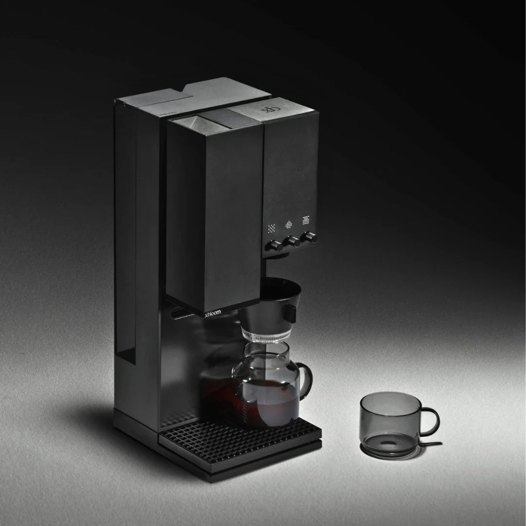 Black coffee brewer with glass dripper and small glass cup beside it