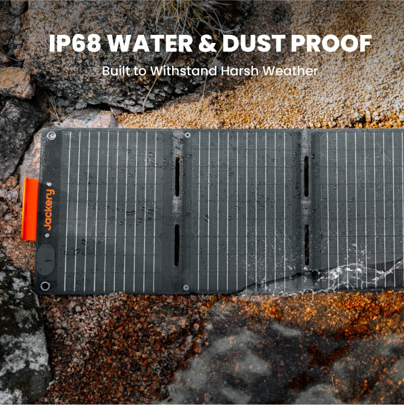 Waterproof solar panel with orange Jackery logo on rocks, water-spray visible