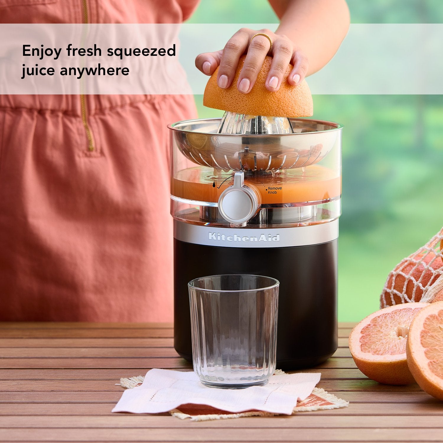 Black citrus juicer dispensing juice as hand squeezes orange over clear strainer