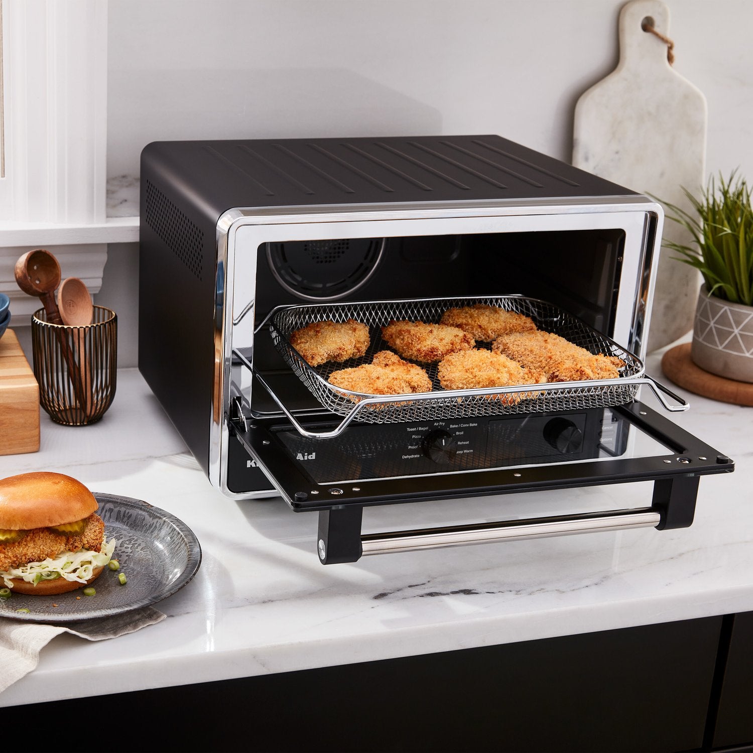 Black matte countertop oven with open door and wire basket holding browned food