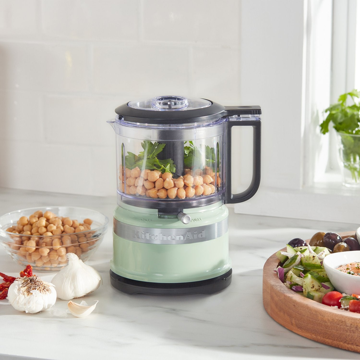 Food chopper with clear bowl filled with light ingredients, mint base, and black lid