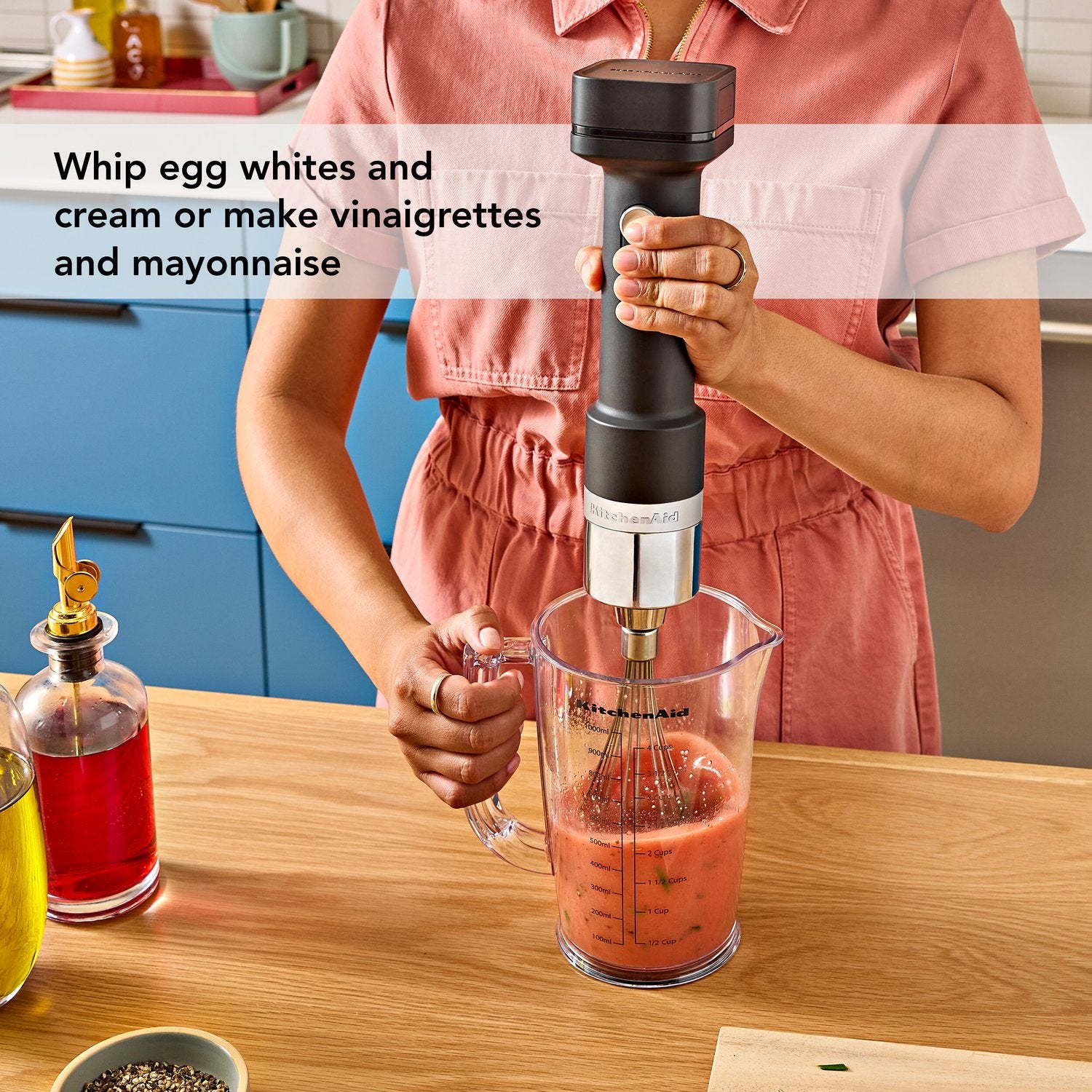 Black matte cordless hand blender whisking in a clear measuring cup.