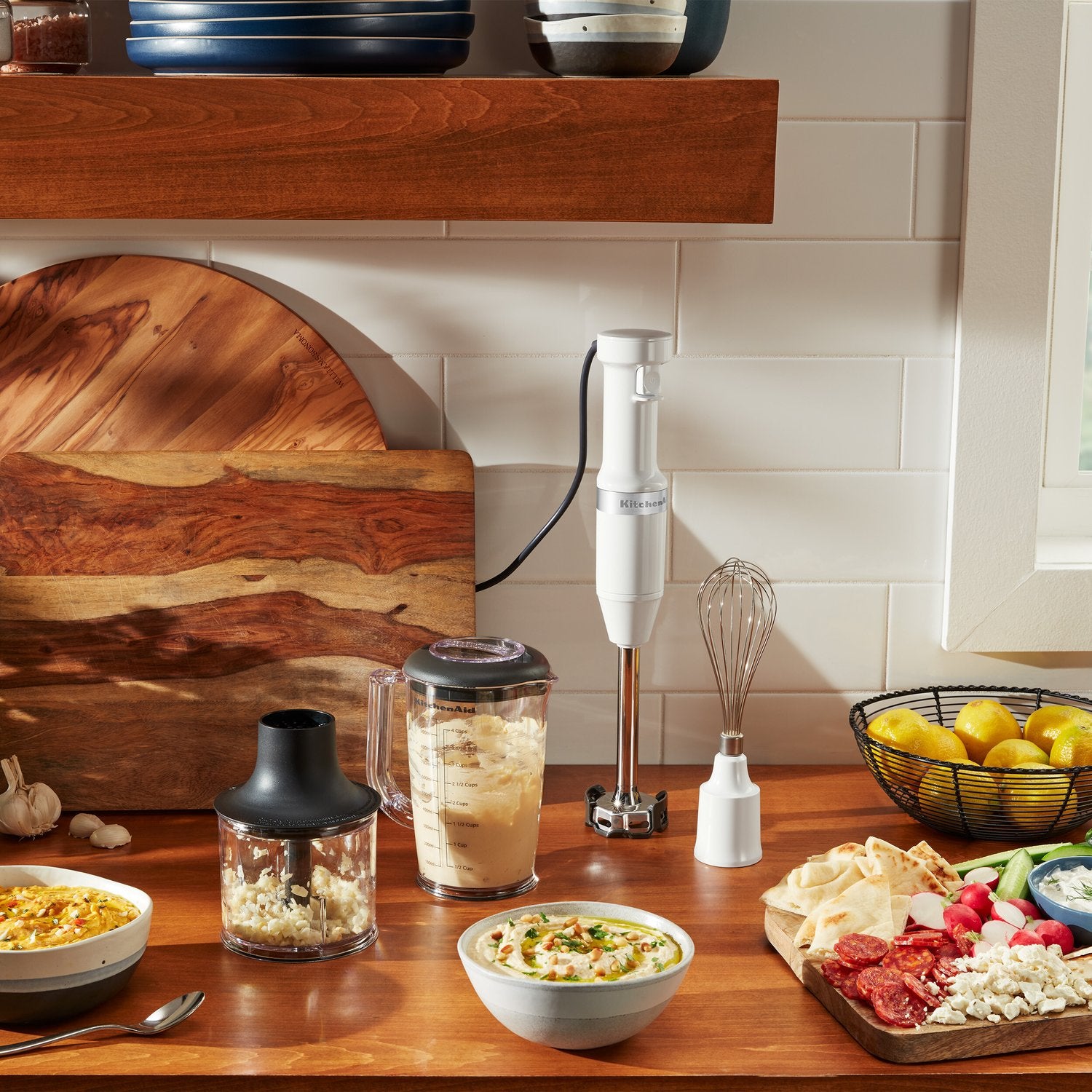 White immersion blender with blending jar and whisk on kitchen counter