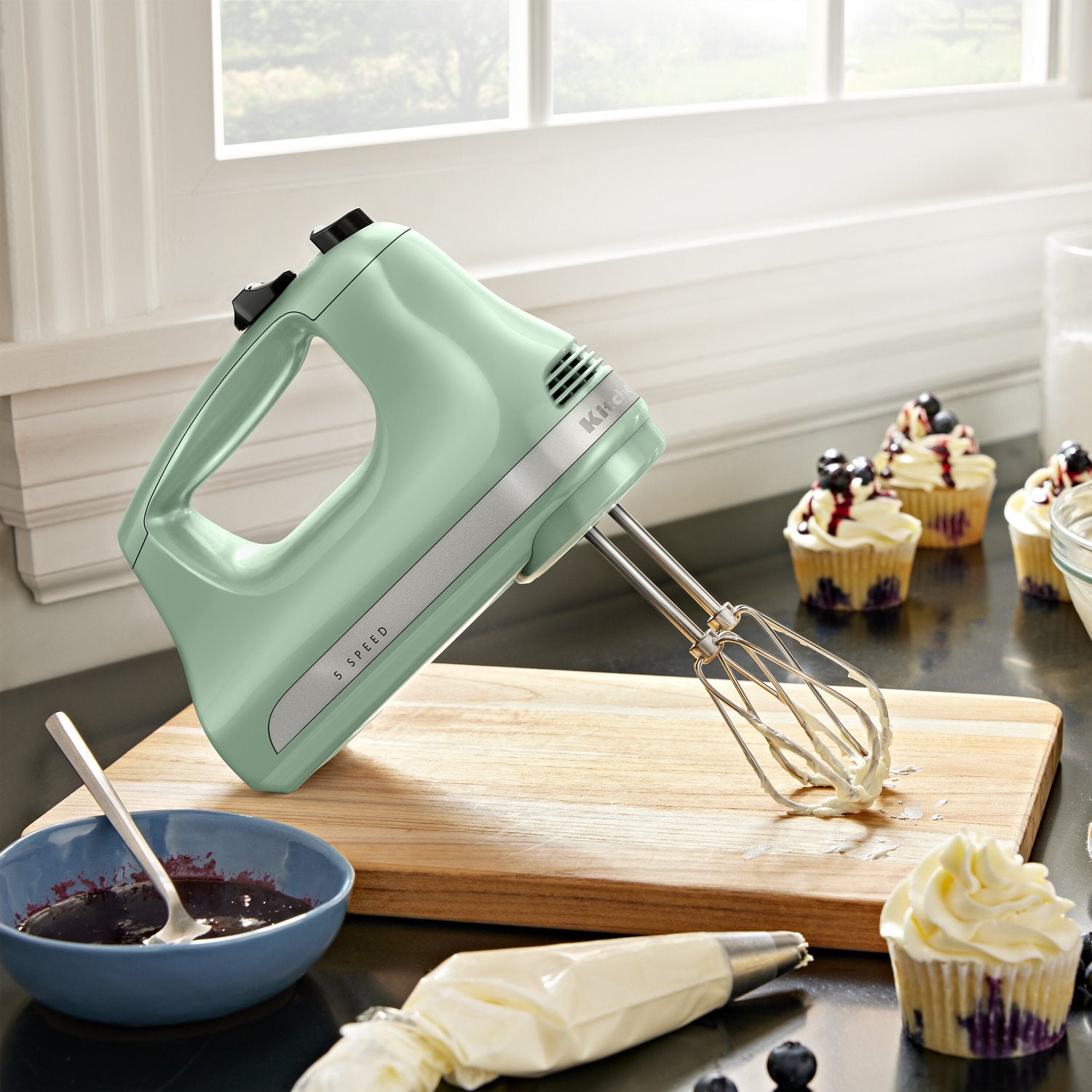 Pistachio green hand mixer with beaters whipping batter on board