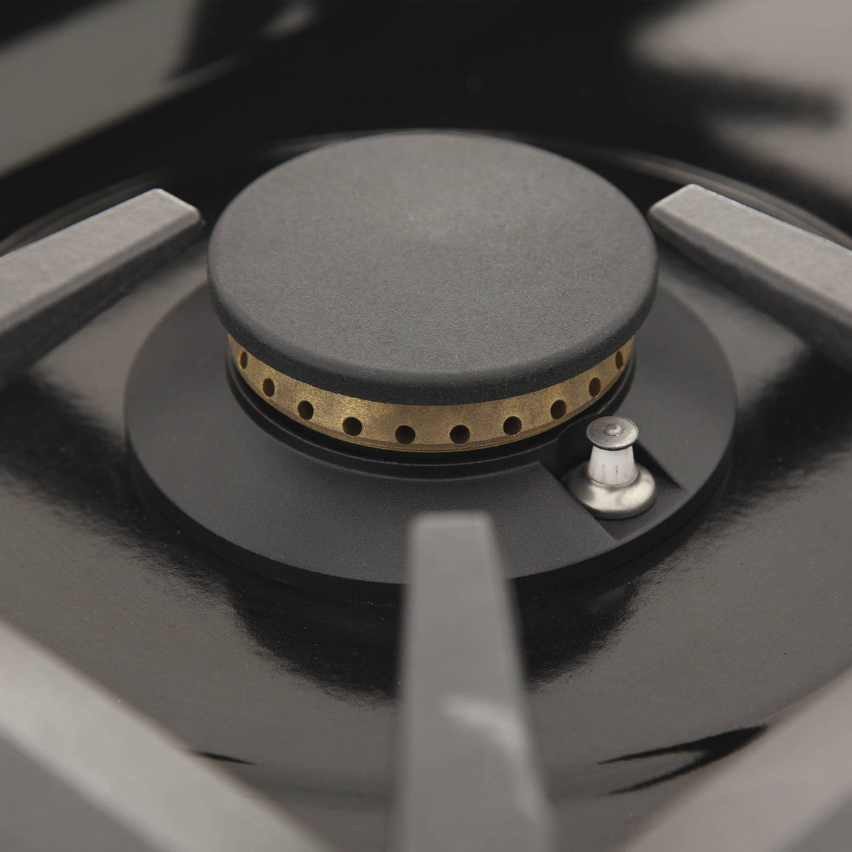 Black gas burner head with round cap and flame ports on cooktop