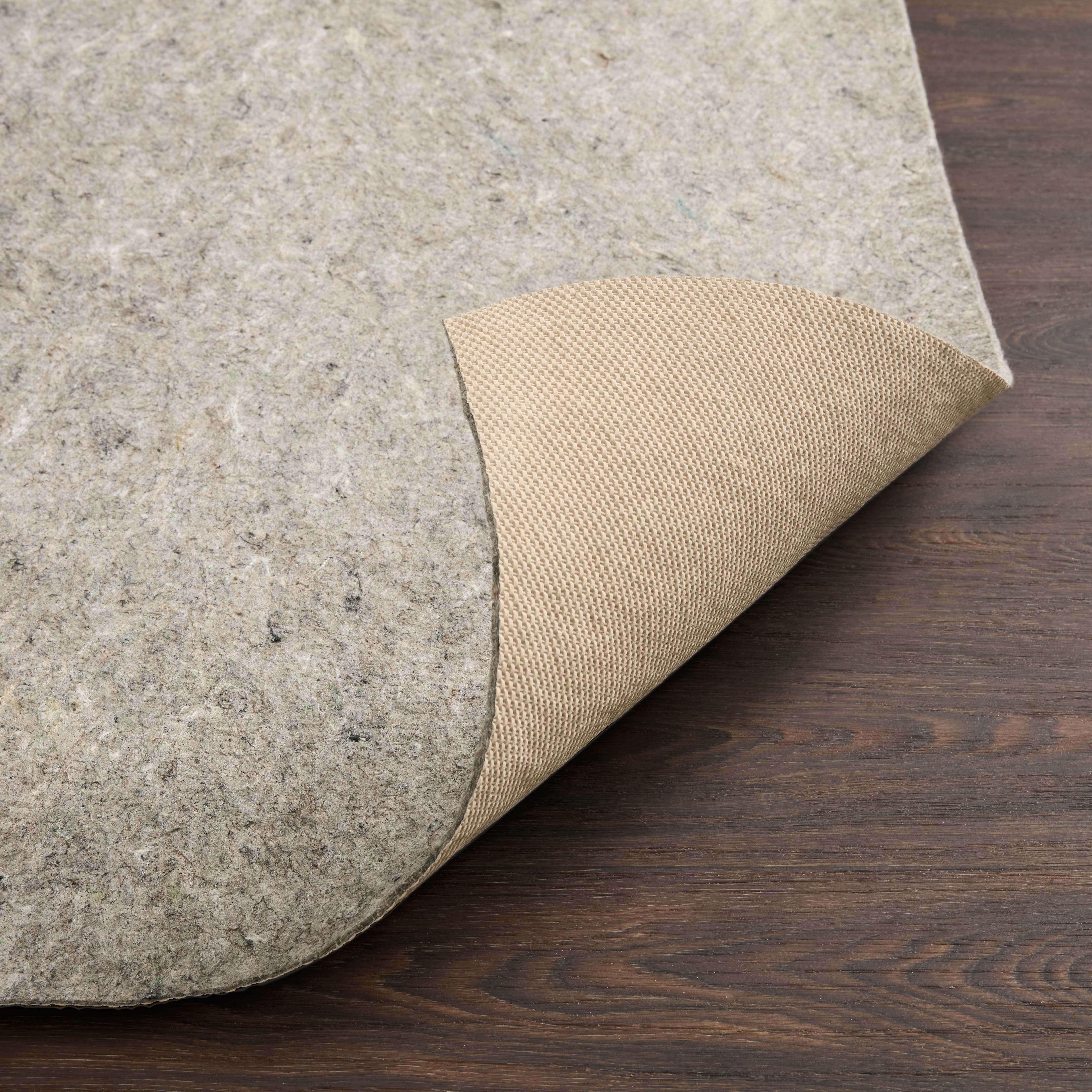 Grey rug pad corner showing beige woven grip backing on dark wood floor.