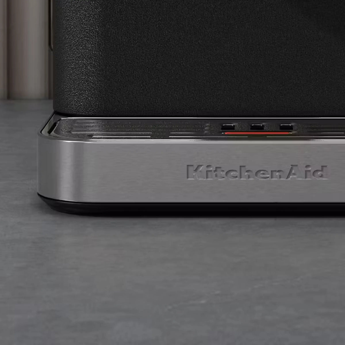 Close-up of black espresso machine base with KitchenAid logo and control lights.