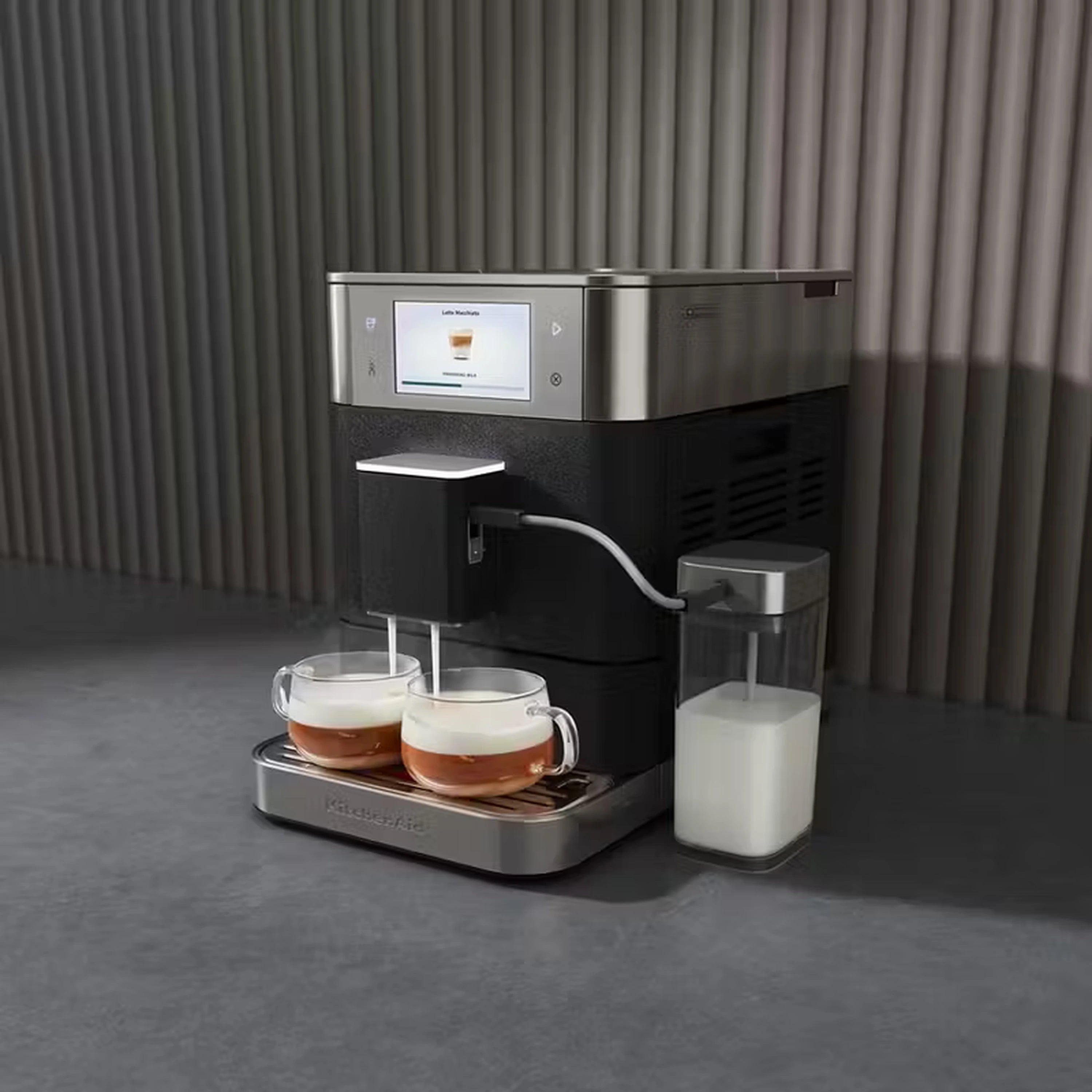 Stainless fully automatic espresso machine on countertop with cup, drip tray, and milk container