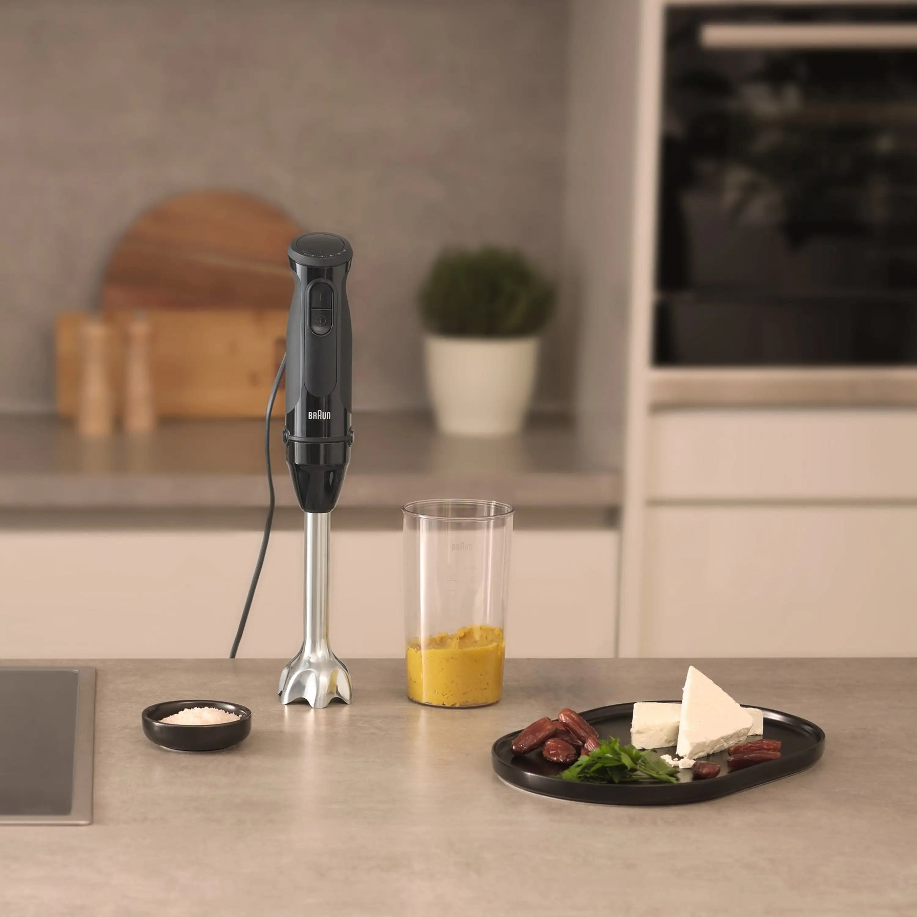 Braun black hand blender with blending shaft, shown blending ingredients in a cup