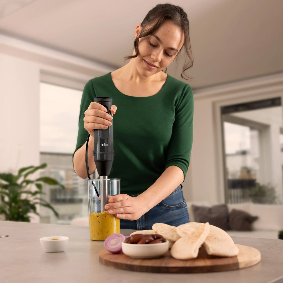 Braun black hand blender used to blend yellow puree in a clear cup