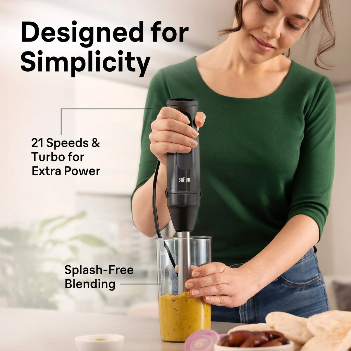 Braun hand blender in use above a clear cup of blended yellow mixture