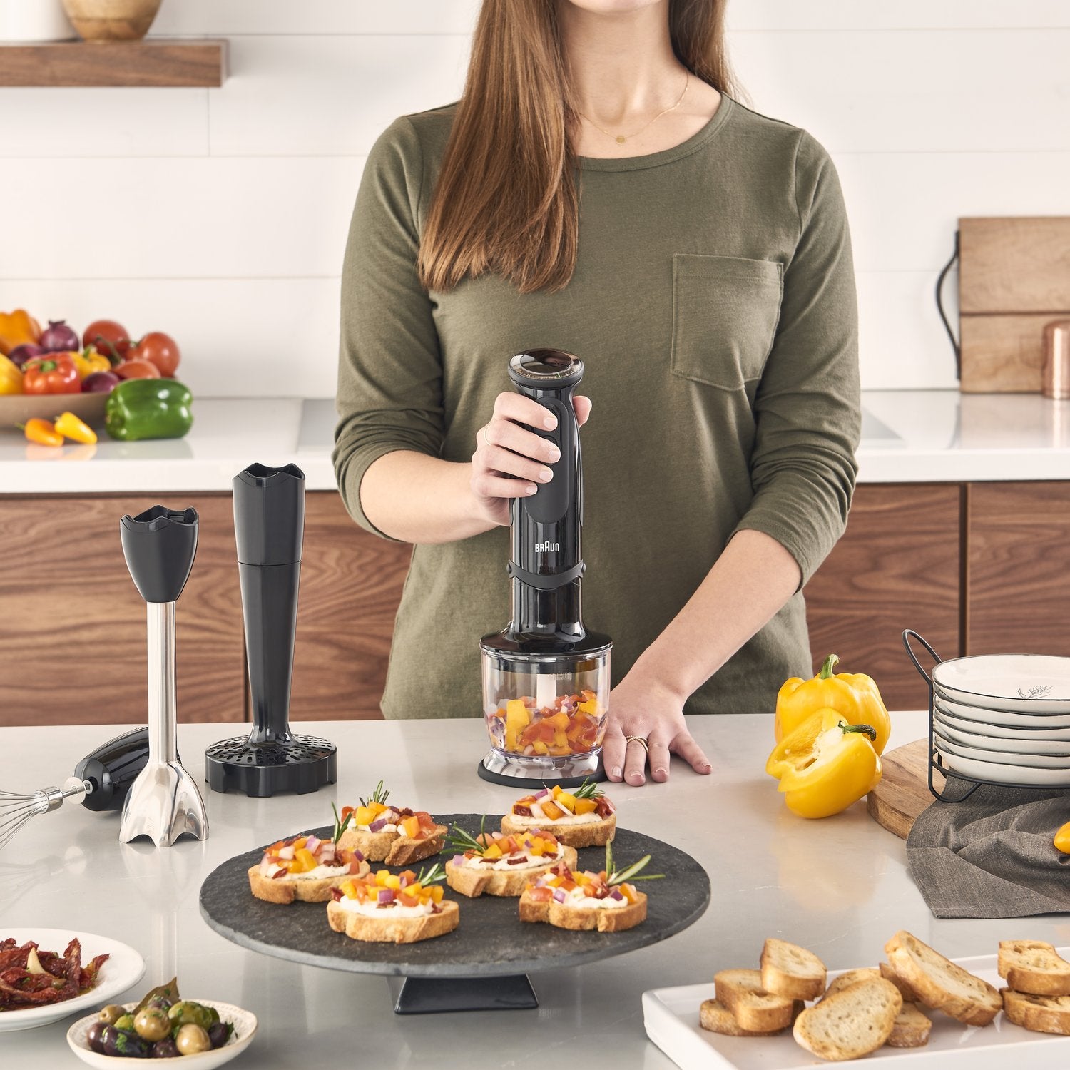 Black hand blender with whisk attachment, held over chopped food for mixing