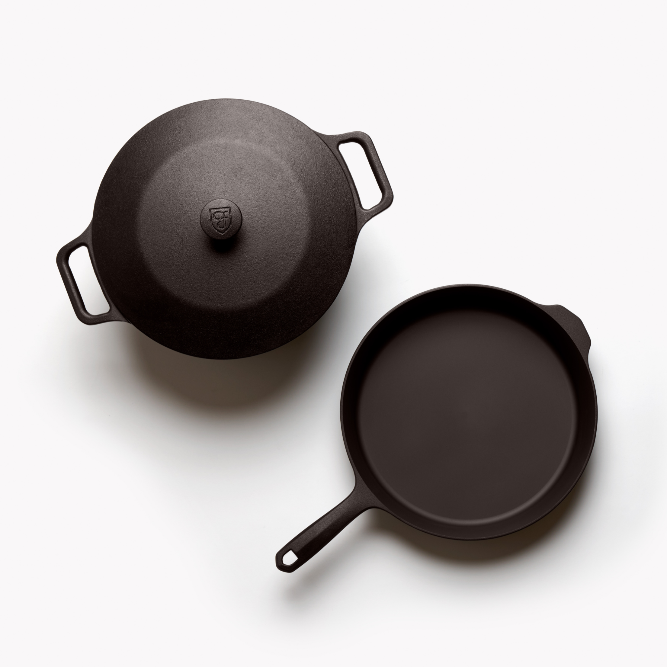 Two cast-iron cookware pieces, lids and handles visible in dark finish