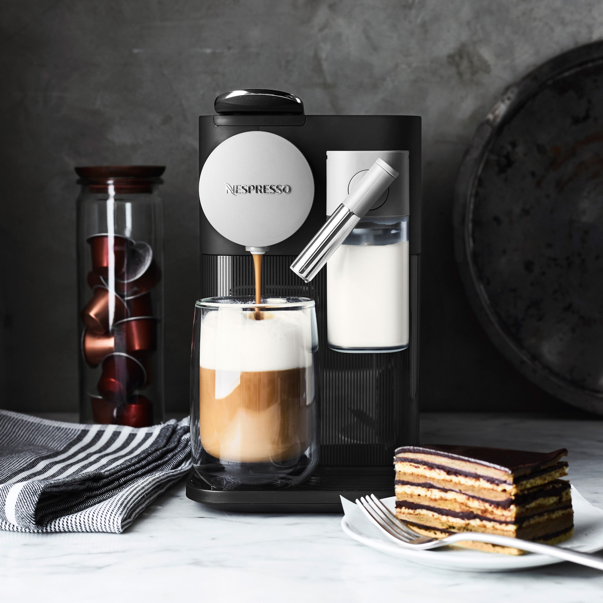 Black Nespresso espresso machine with frothing wand and latte in clear glass