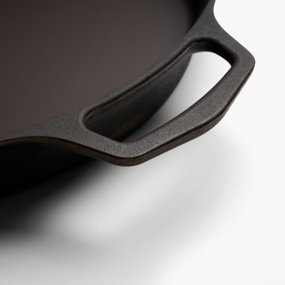 Cast iron skillet side handle detail with matte black finish and curved grip