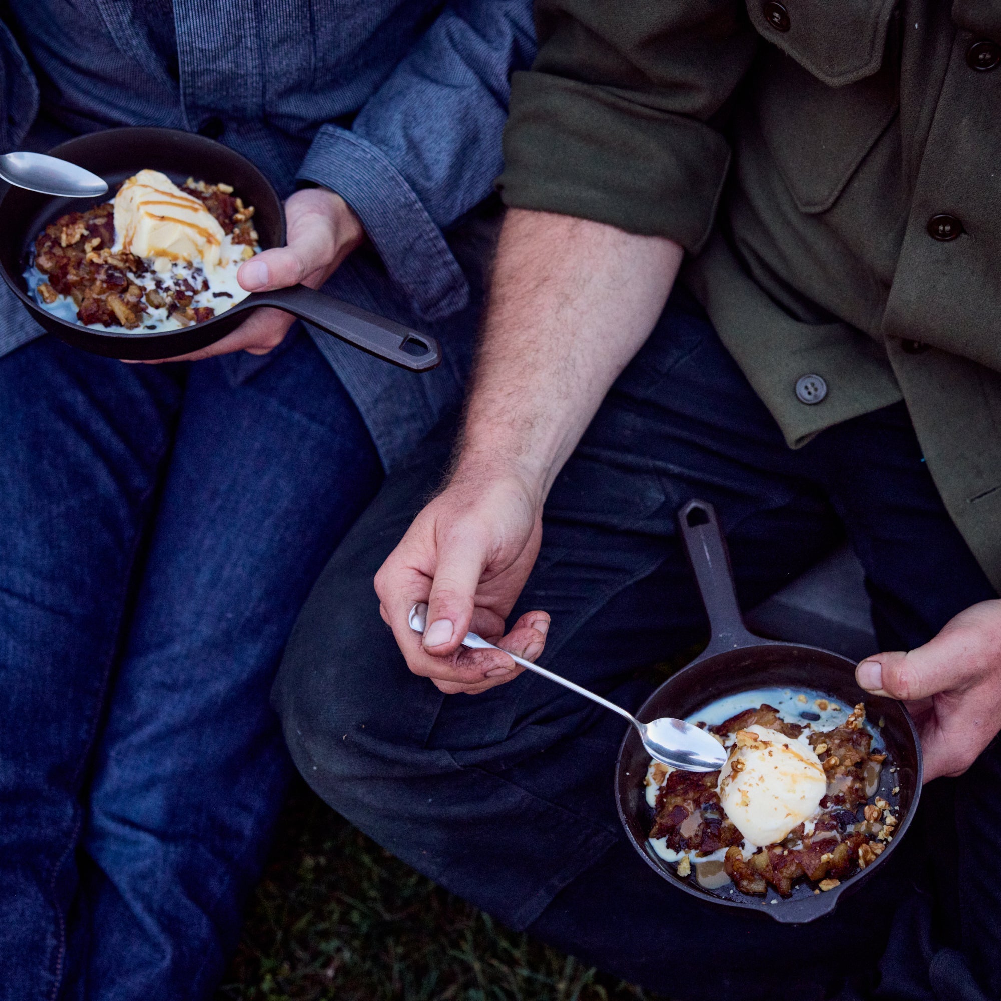 Two dark skillets with handles, filled with food