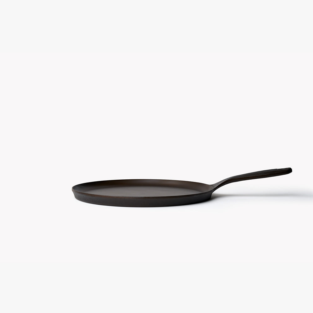Round cast iron griddle, dark finish, short handle, side view