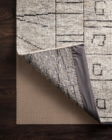 Beige textured area rug with geometric blocks and dark corner binding, stitched edge