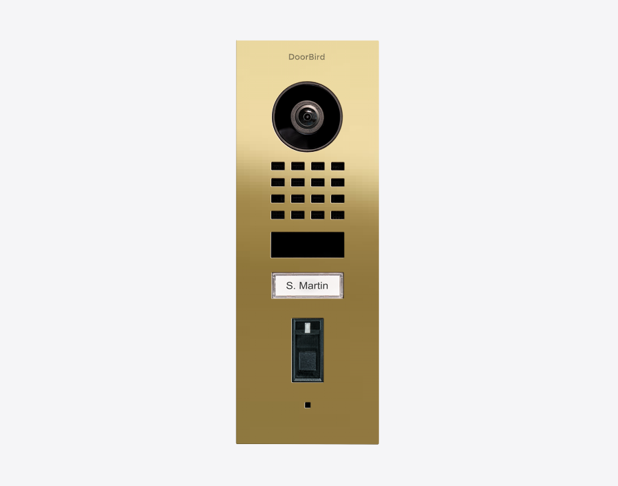 DoorBird flush-mount video door station in brass with camera lens, keypad, name plate