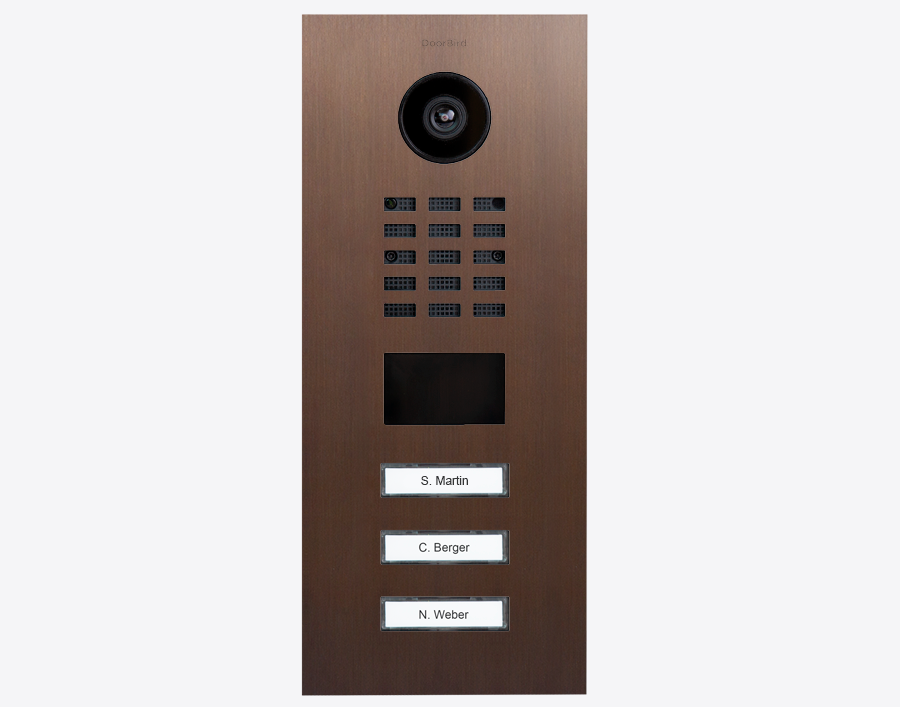 DoorBird video door station with camera, speaker grille, and name label buttons on bronze panel