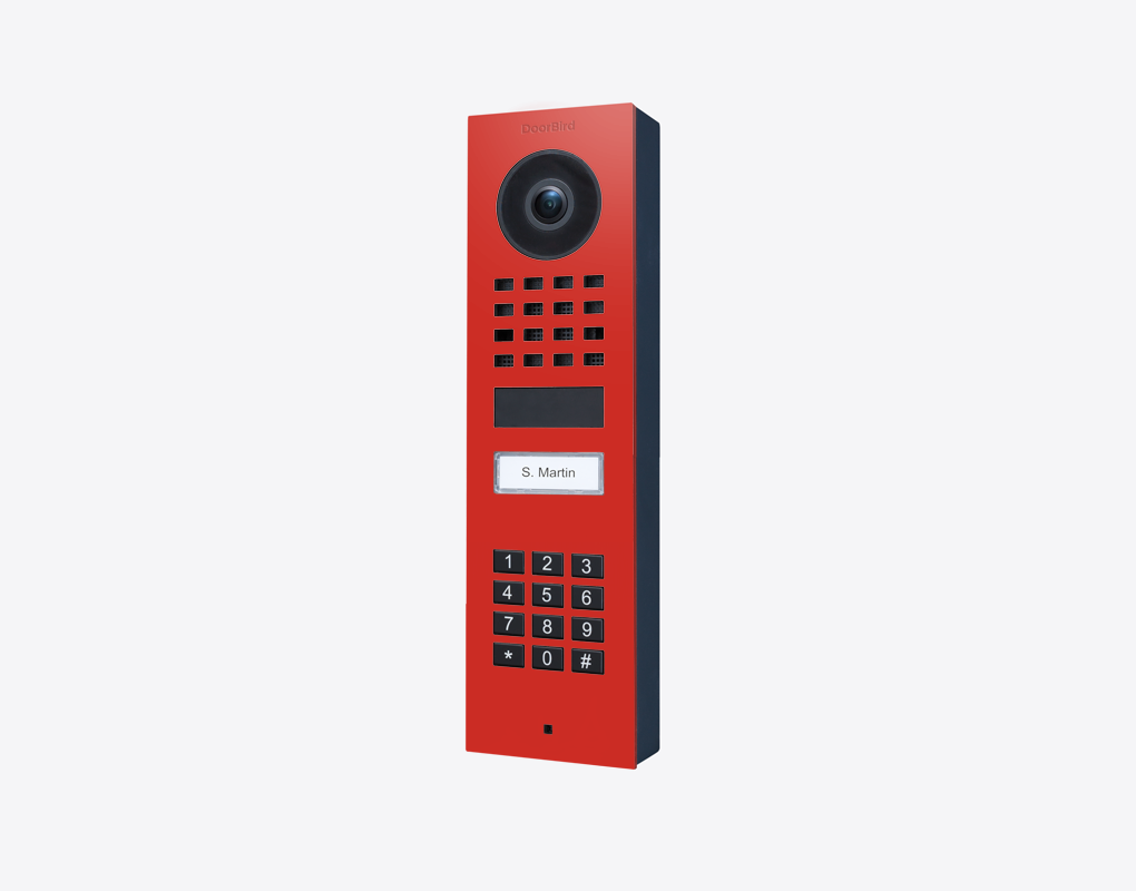 DoorBird surface-mount video door station in pure red with camera lens and keypad