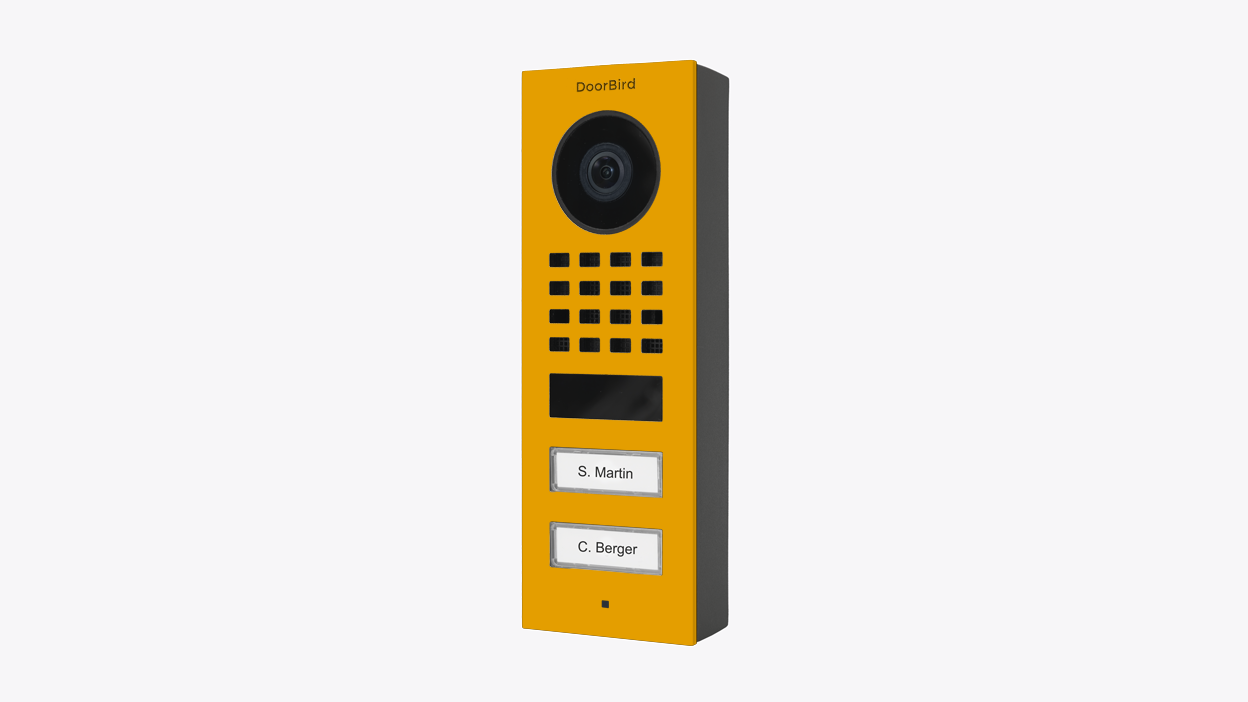 DoorBird video door station in golden yellow with camera lens, speaker grille, and name buttons