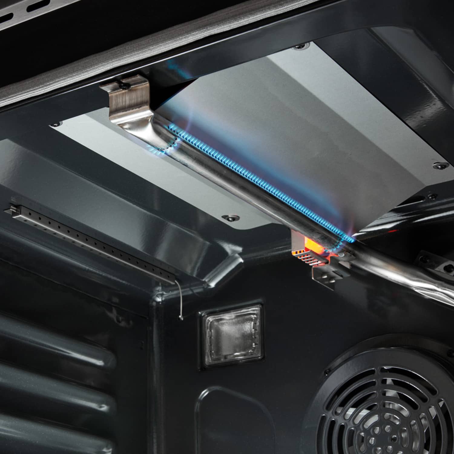 Gas oven burner area with blue flame inside the stainless steel oven