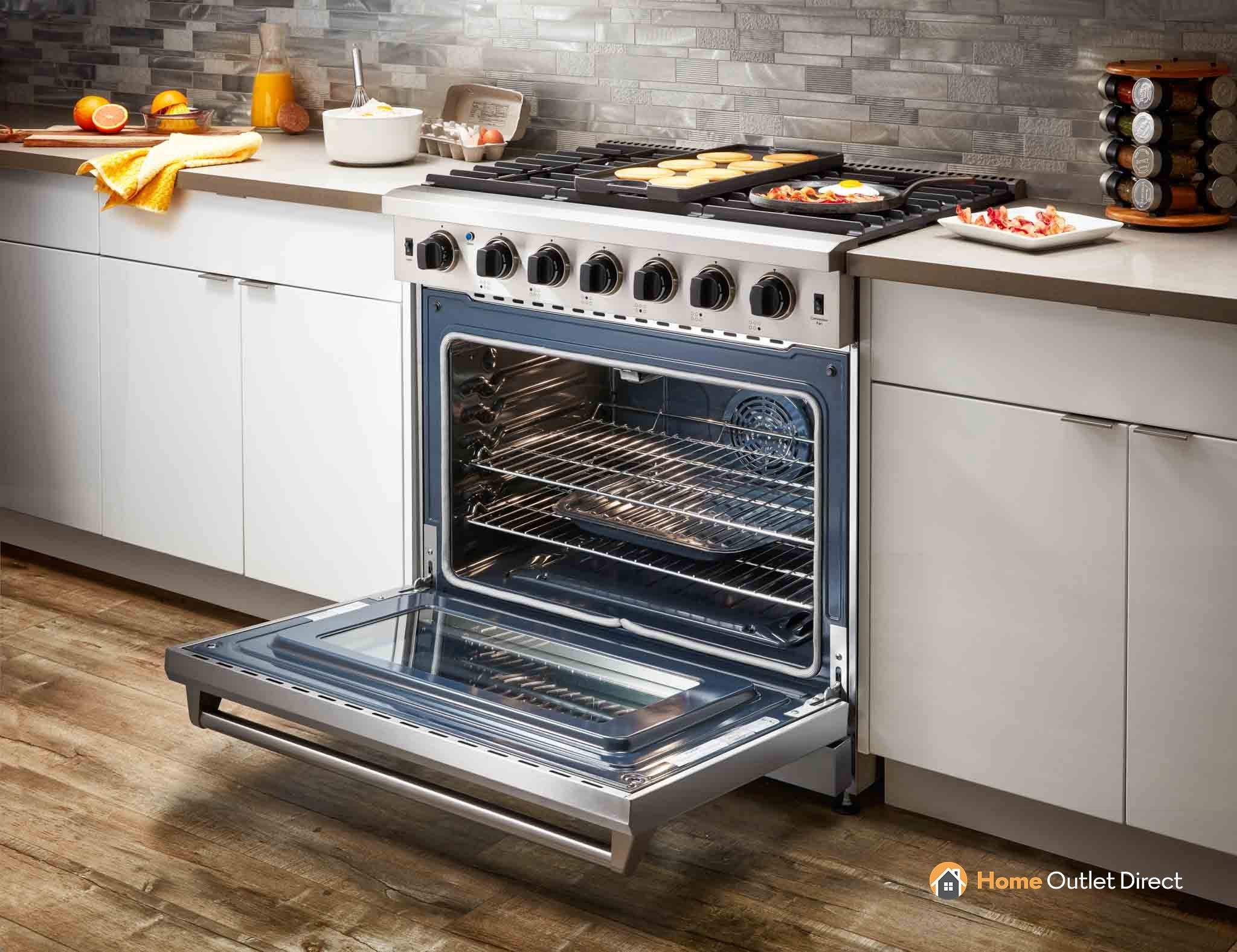 Stainless steel gas range with open oven and flat metal broiler tray on floor