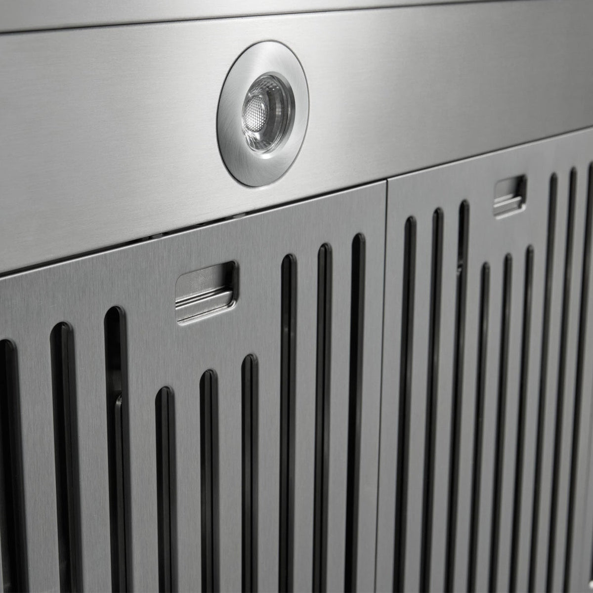 Stainless steel range hood front with vent slots and centered round light