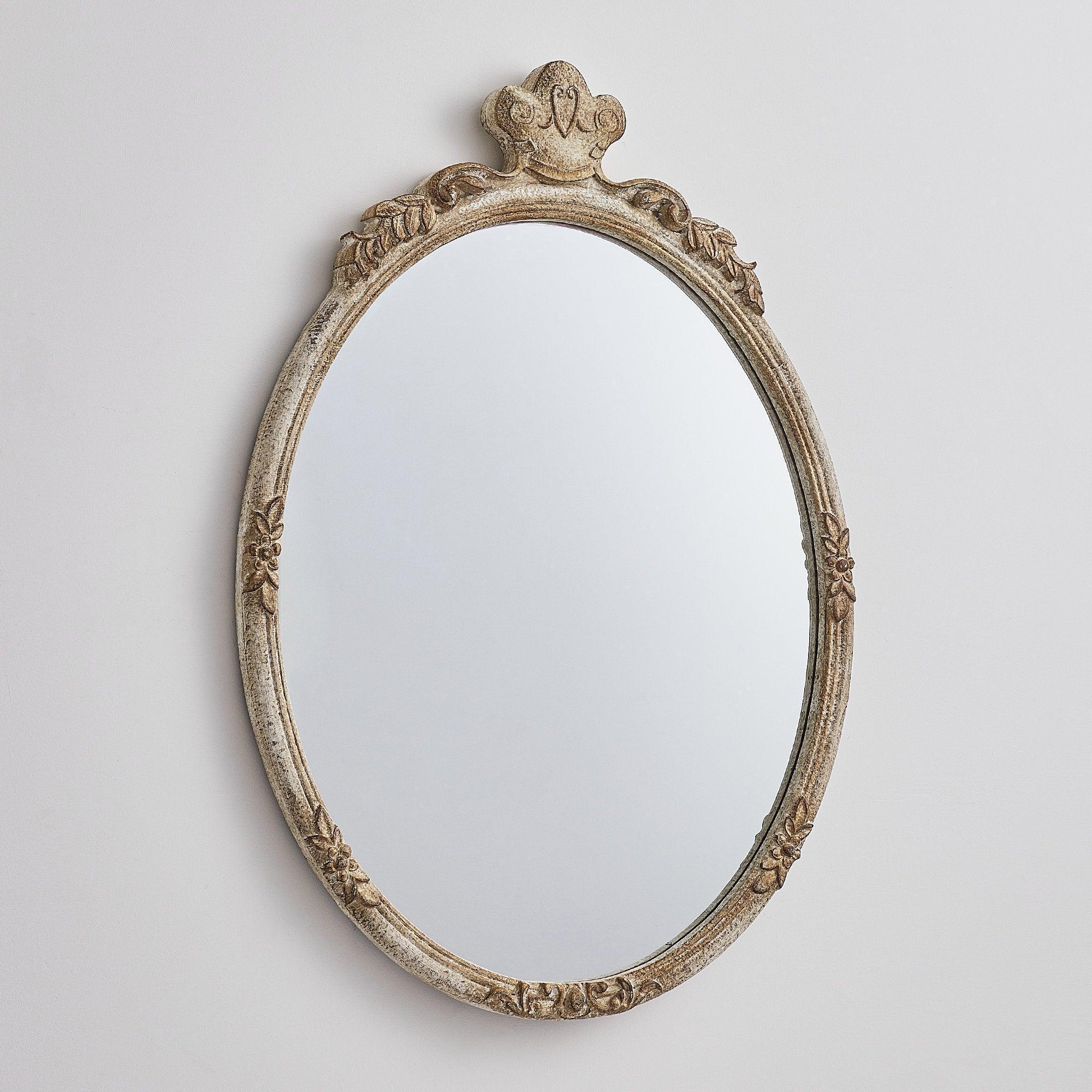 Oval wall mirror with distressed wood frame, ornate leaf border, and crown crest.