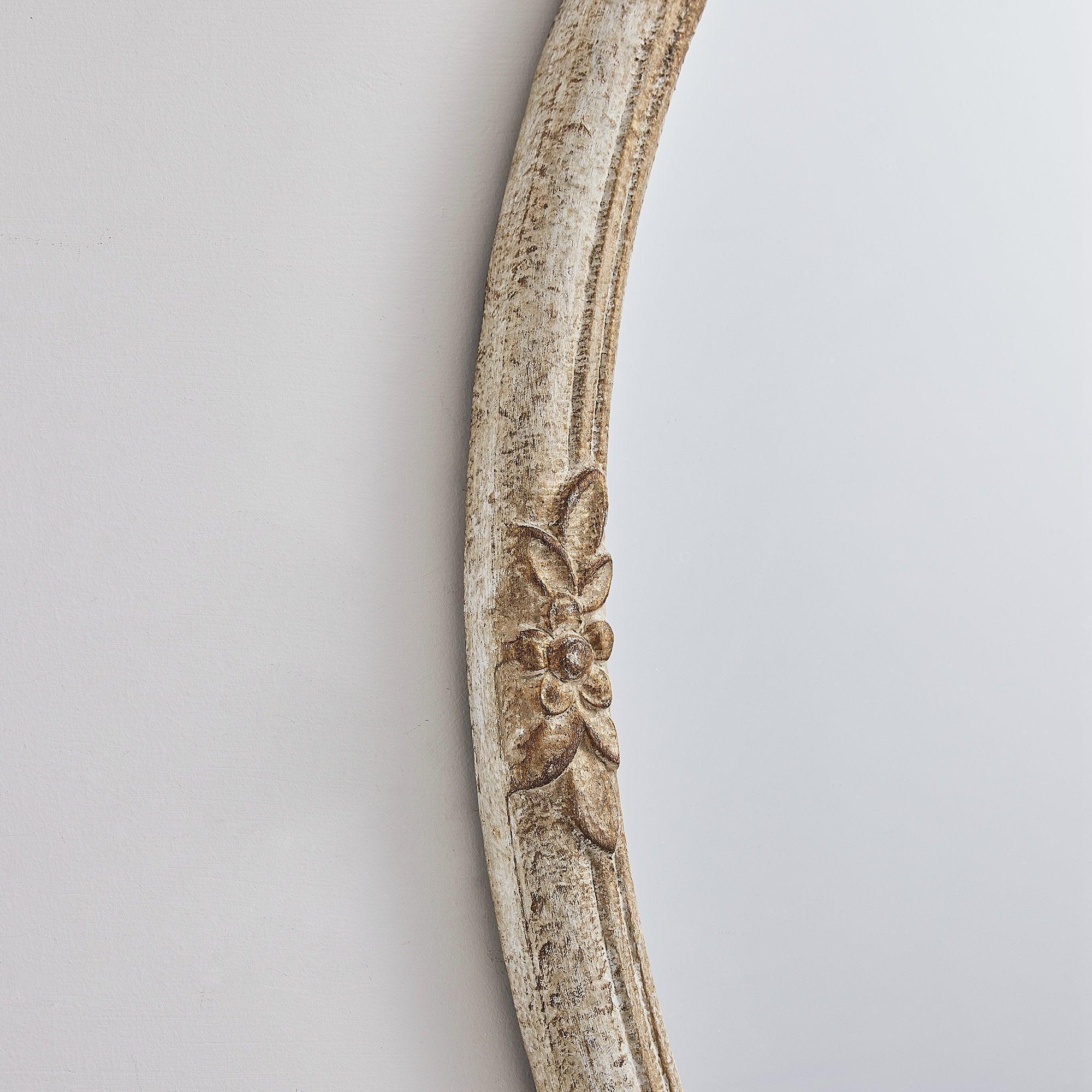 Close-up of distressed wood oval mirror frame with carved leaf detail.