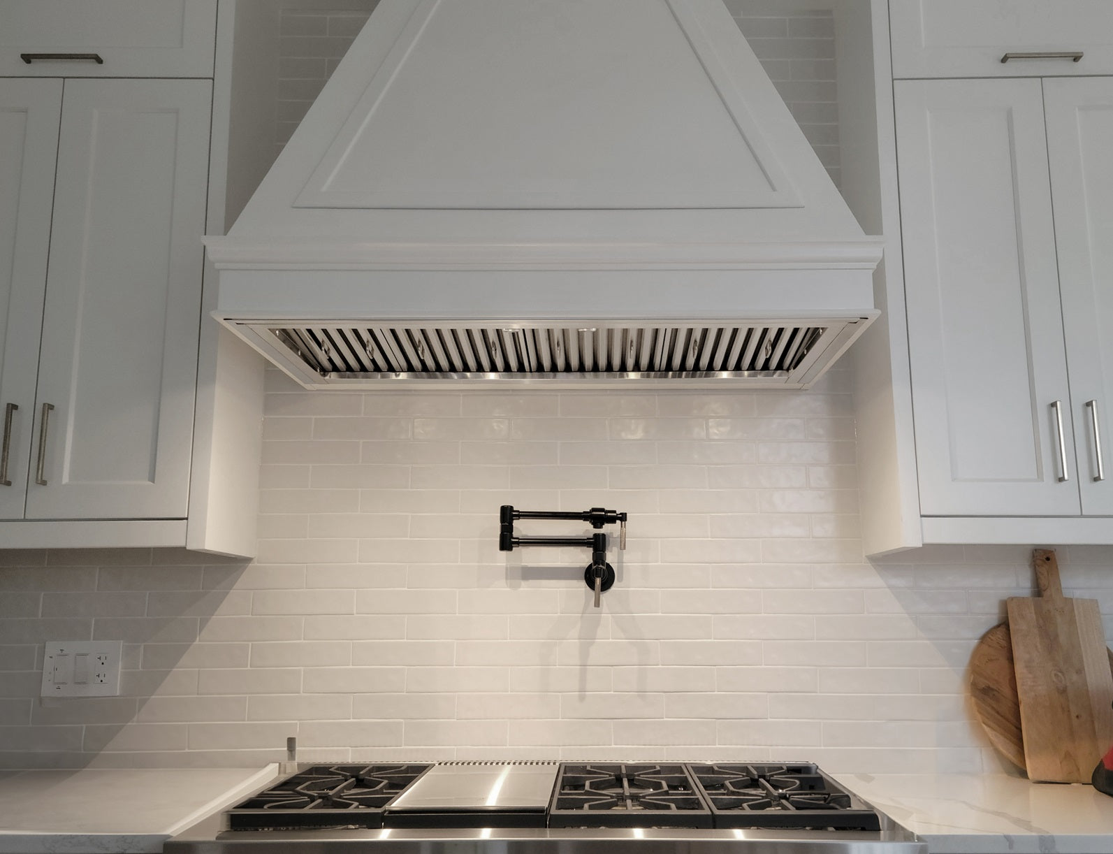 Stainless steel insert range hood with vent grille above cooktop, kitchen view