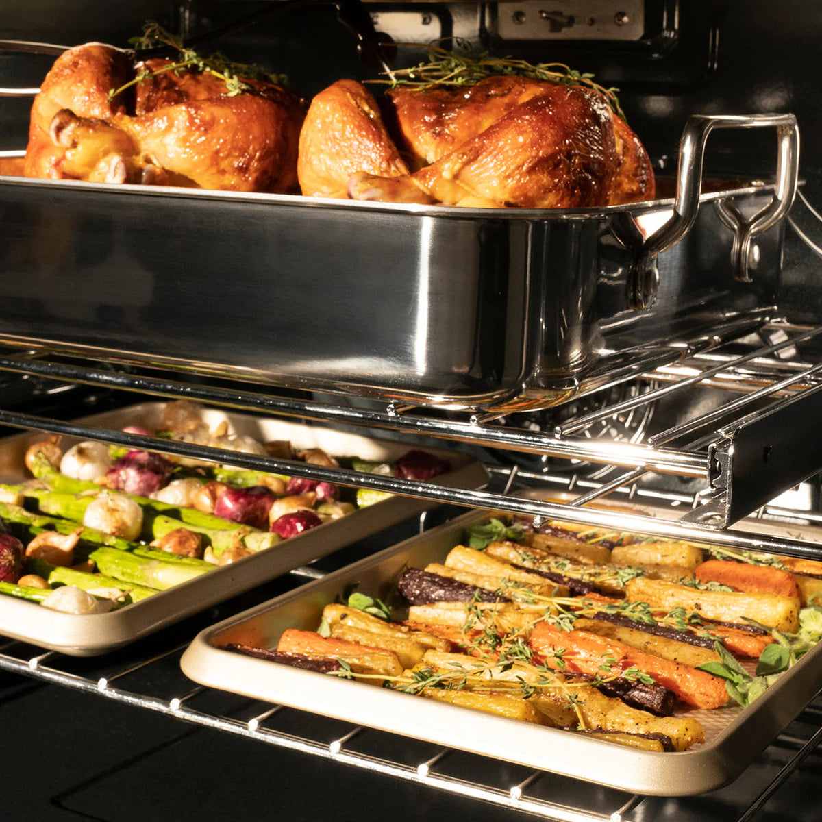 Oven cavity with two racks holding roasted poultry and vegetables on baking trays