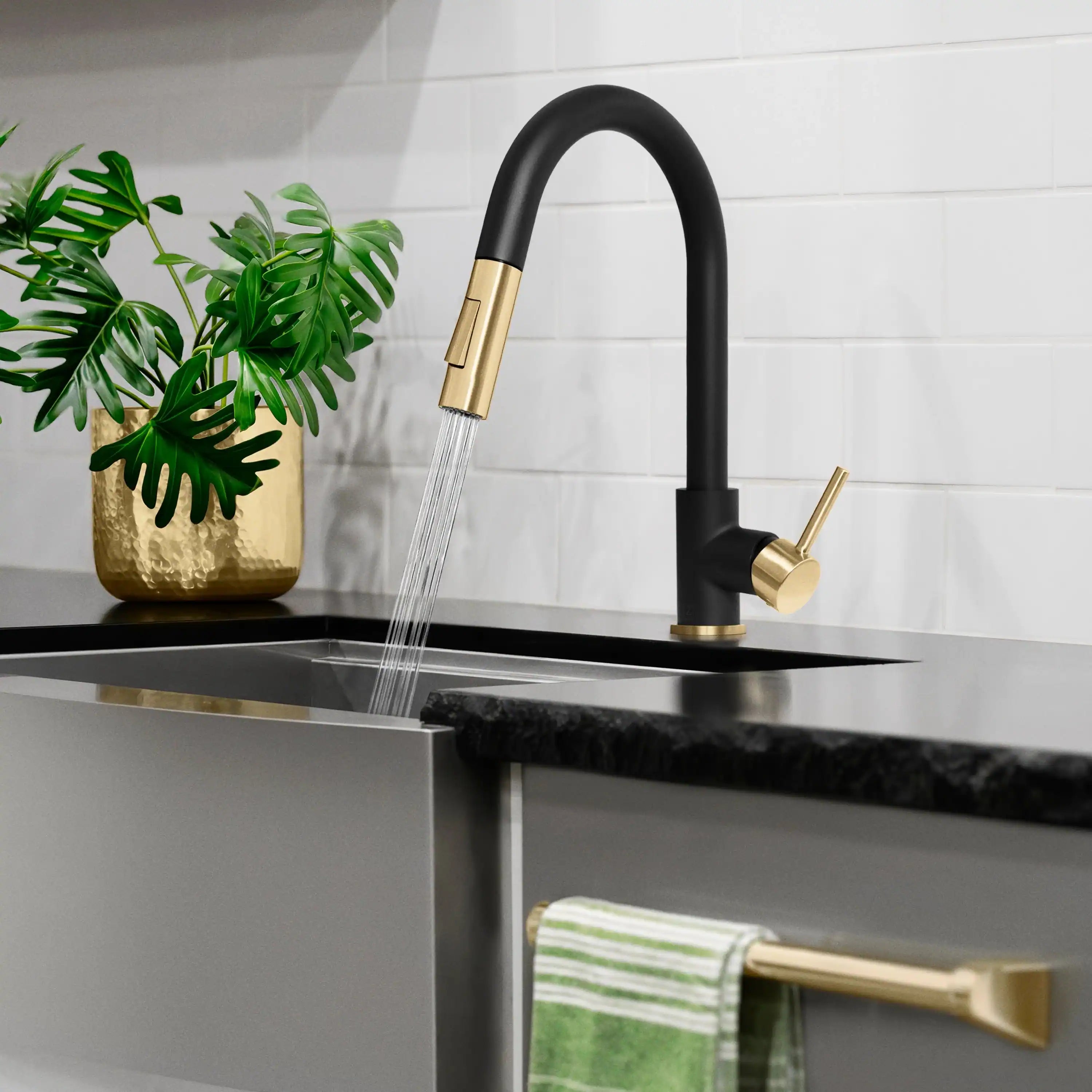 Matte black kitchen faucet with champagne bronze handle dispensing water into sink