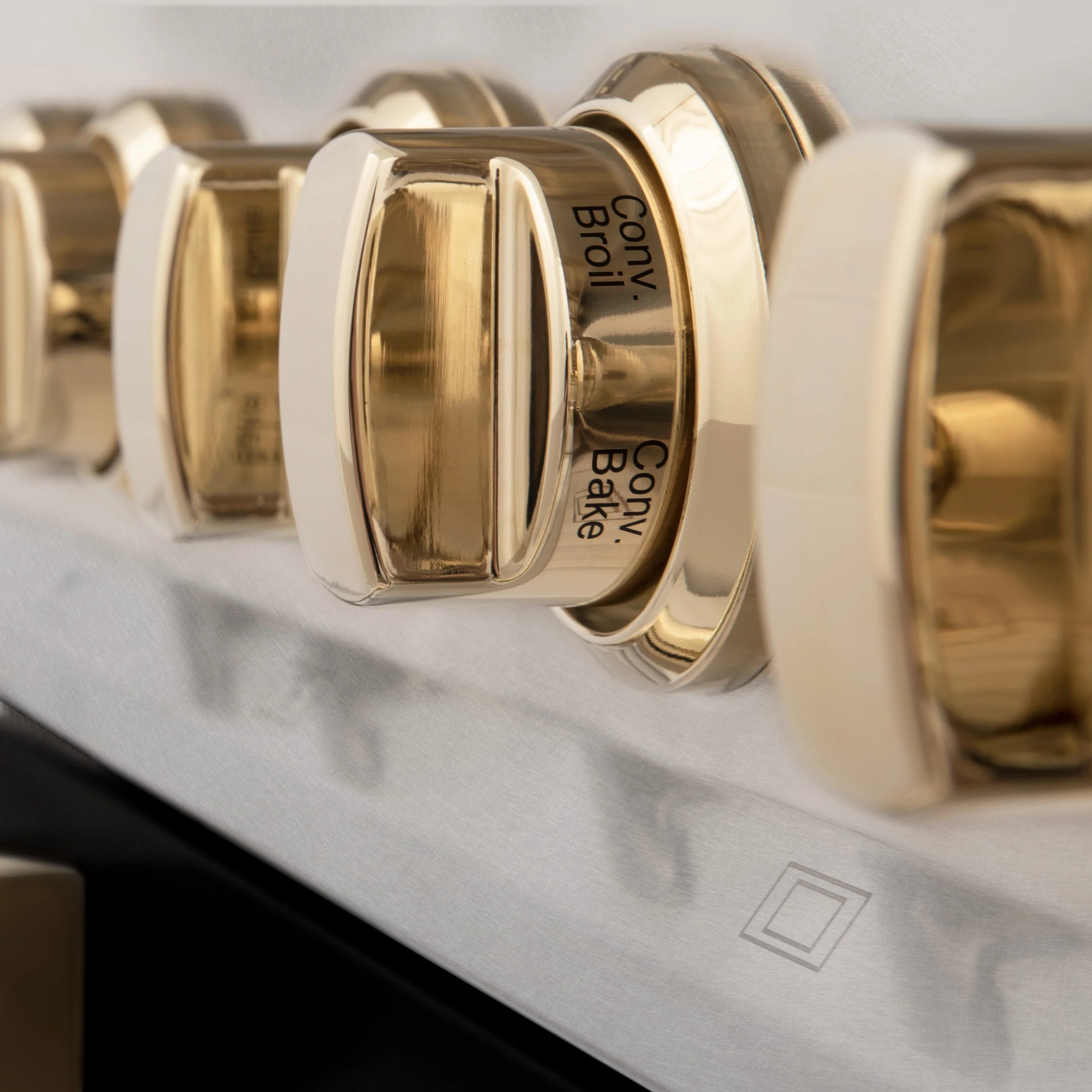 Gold control knob on stainless range panel with labeled settings
