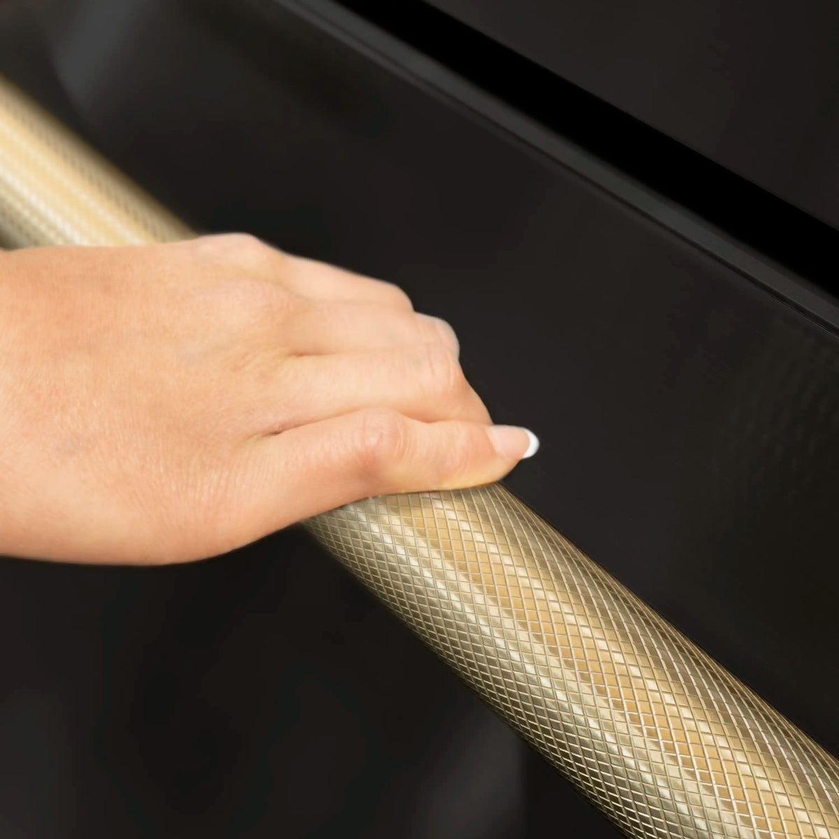 Black refrigerator door with bronze helix handle as a hand pulls