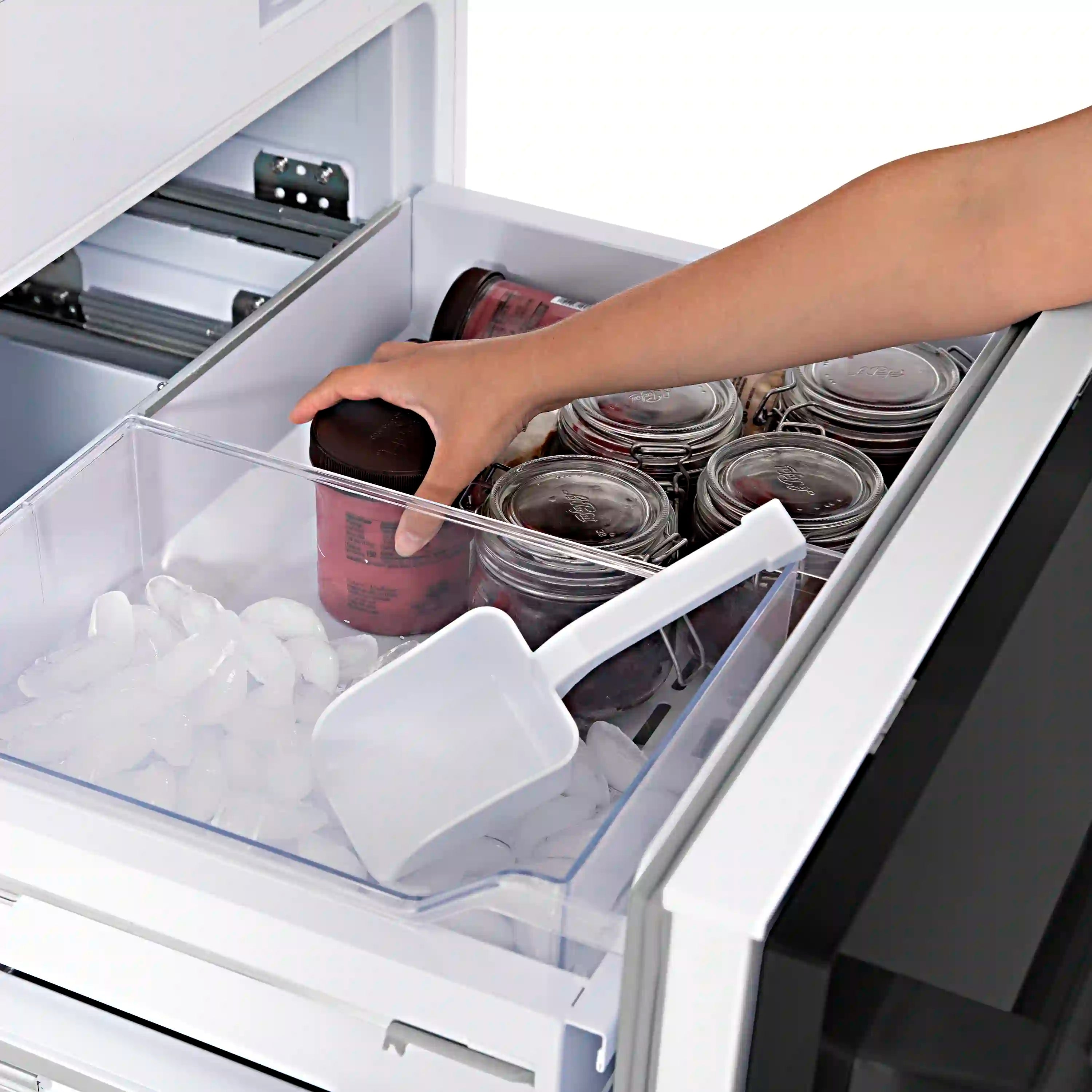 Open bottom freezer drawer with ice tray and hand lifting a container