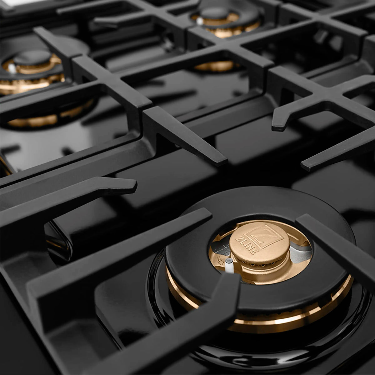 Black gas cooktop grates with a polished gold burner cap, viewed from above