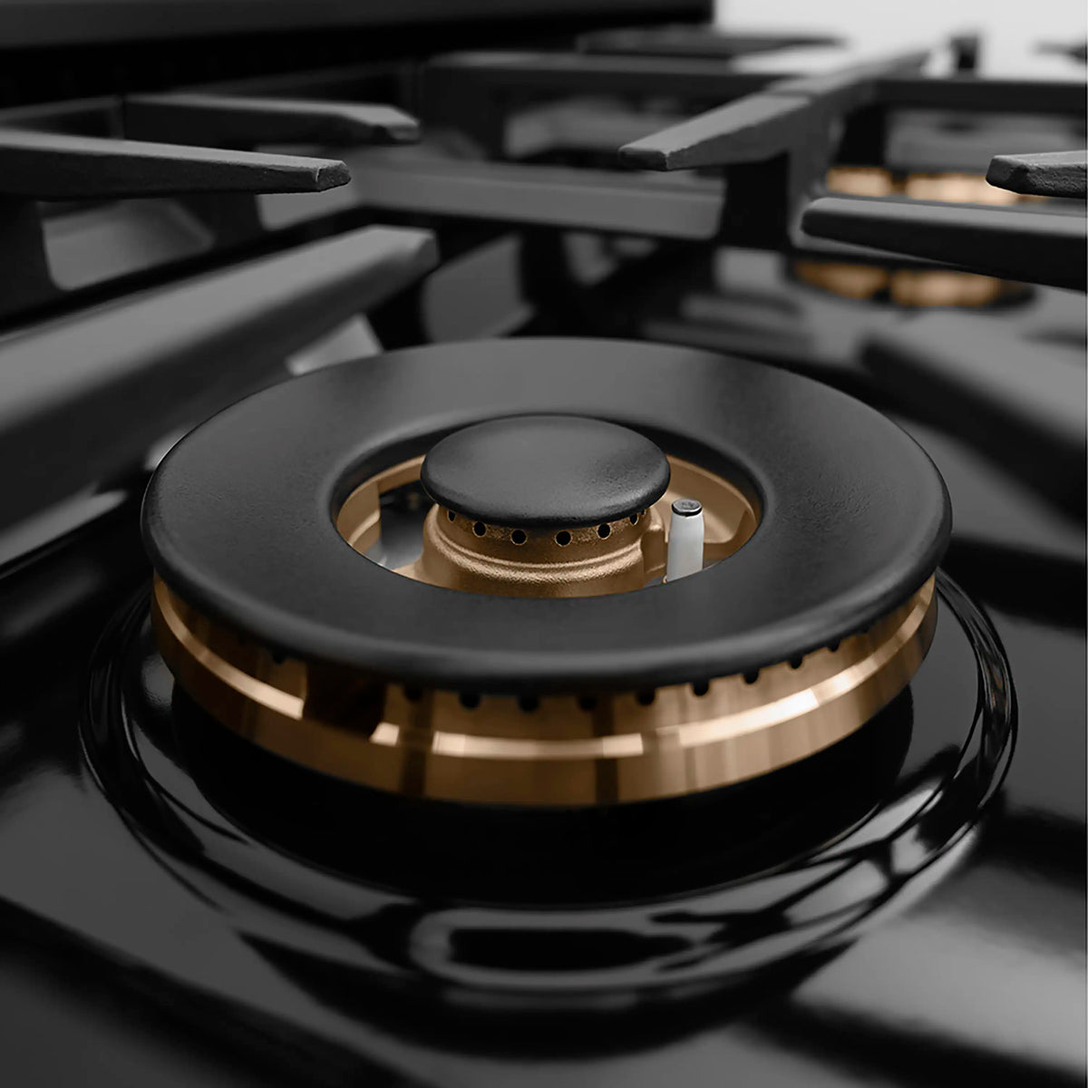 Close-up of a black gas burner head with polished gold ring and flame cap