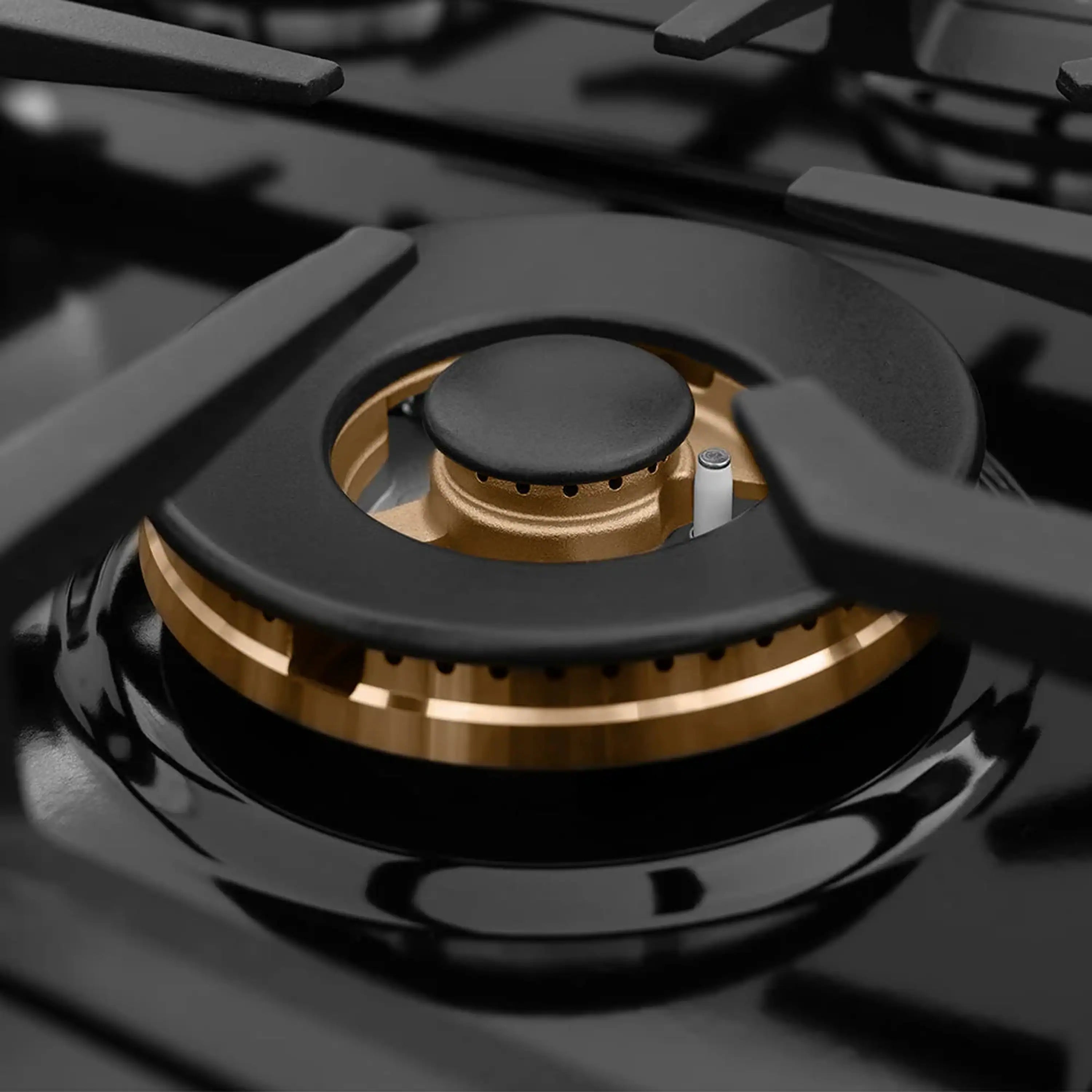 Black gas cooktop burner with dark cap and gold ring on a glossy porcelain surface