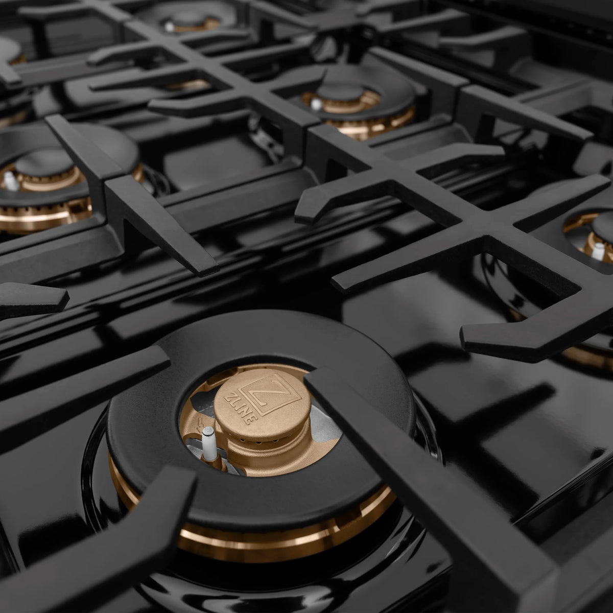 Black cooktop burner with champagne cap and logo center on cast grates
