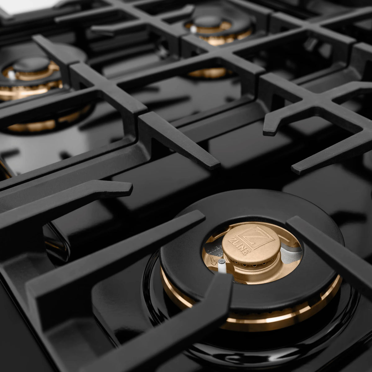 Black cooktop burner head with gold-toned cap and cast burner grate, close-up