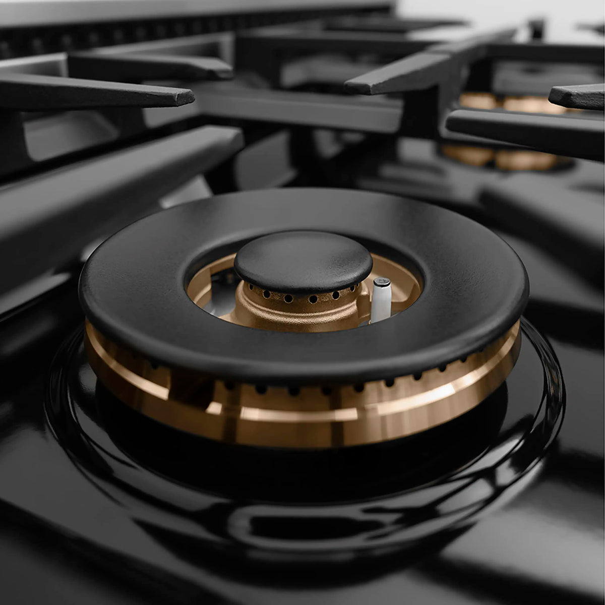 Close-up of black burner head with brass ring on a glossy cooktop surface