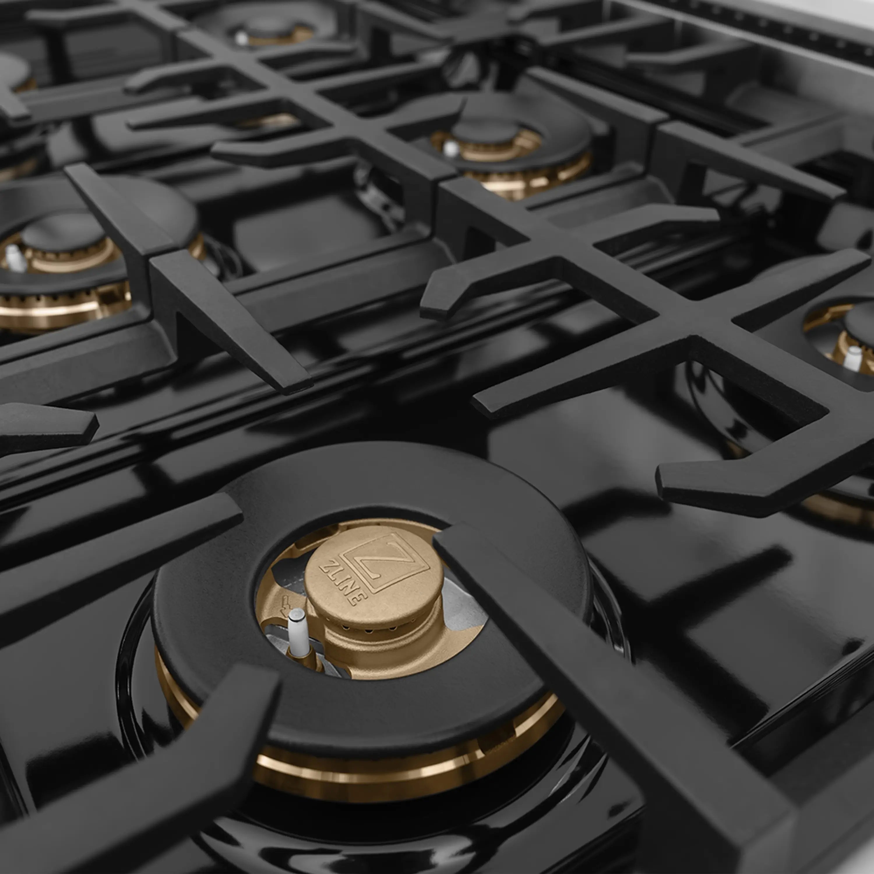 Multiple gas cooktop burners with black grates and gold brass caps