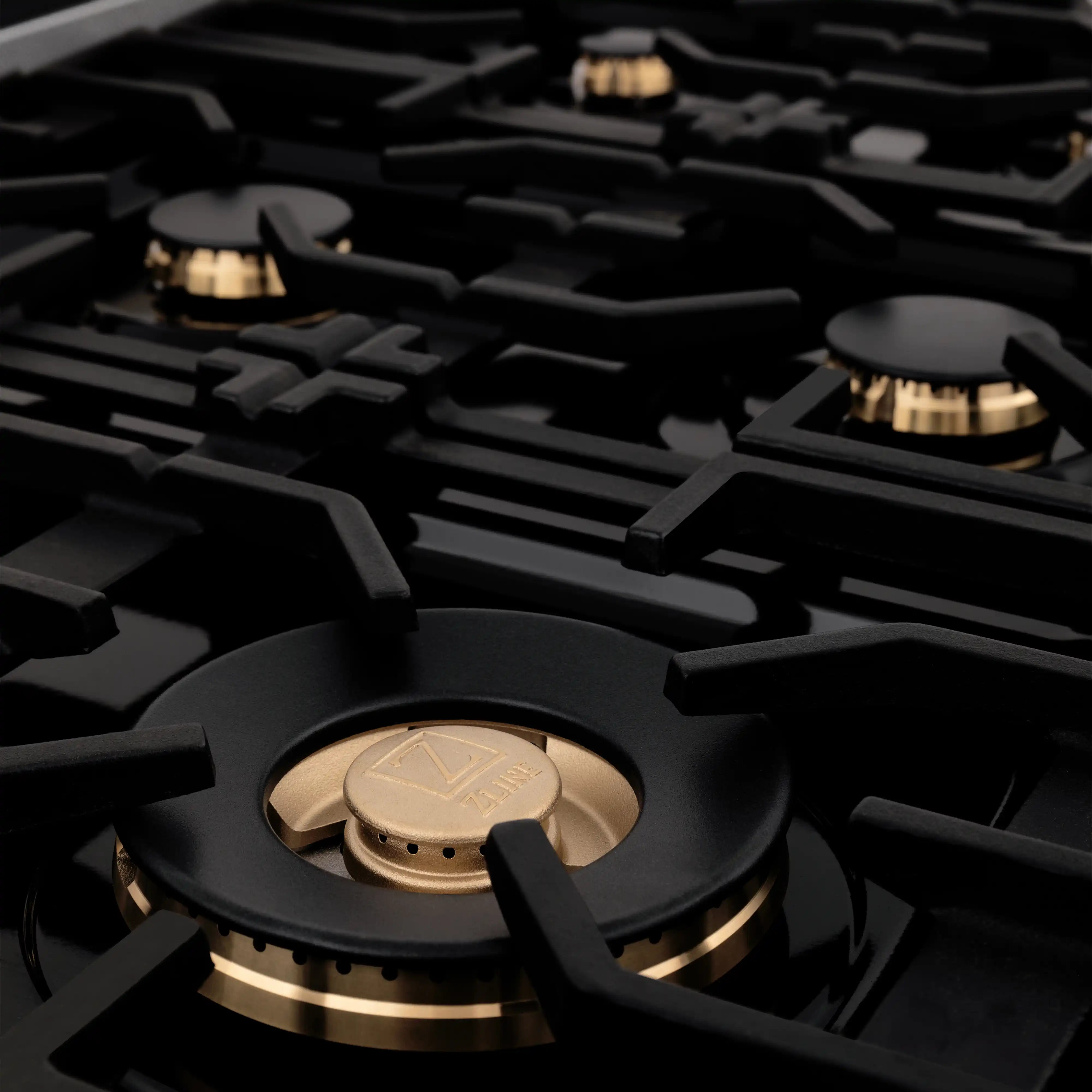 Close-up of black gas burner with gold-toned ring and grates on a dark cooktop
