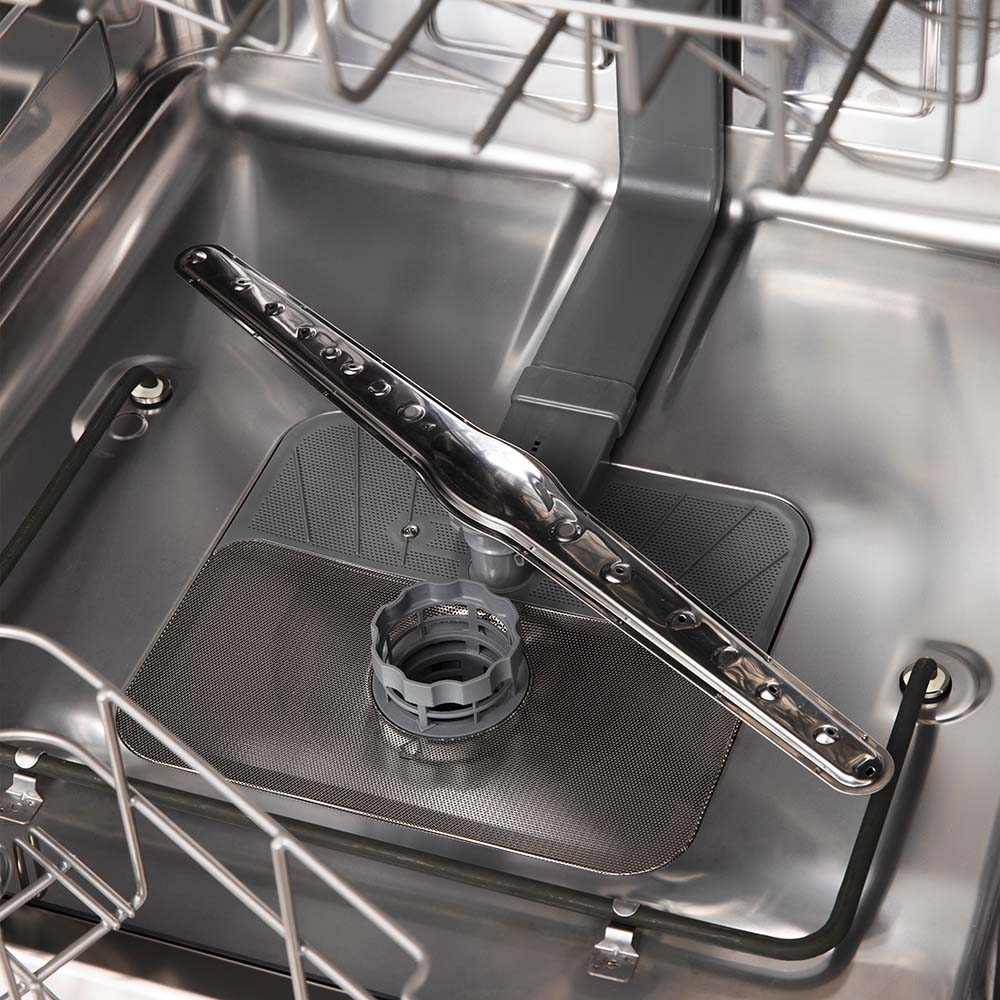 Dishwasher interior with utensil tray and spray arm assembly in stainless tub.