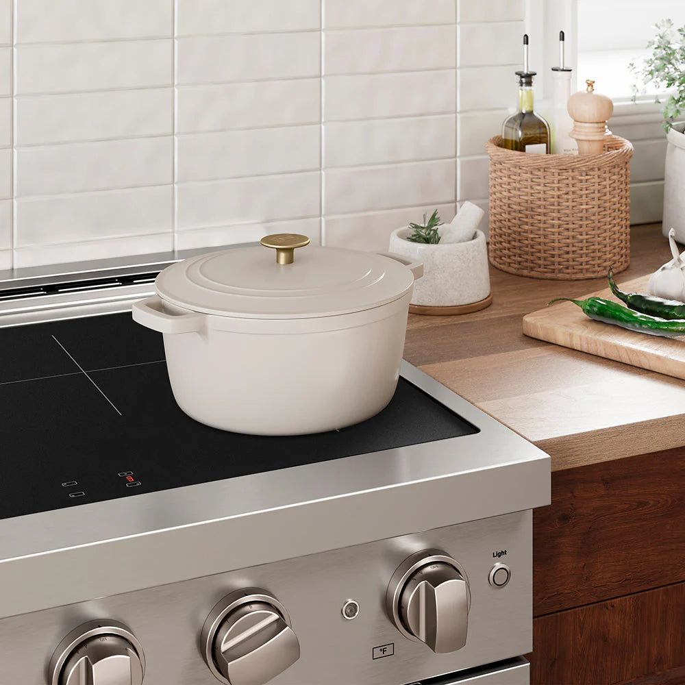 White matte enameled cast iron pot with lid and gold knob on stove