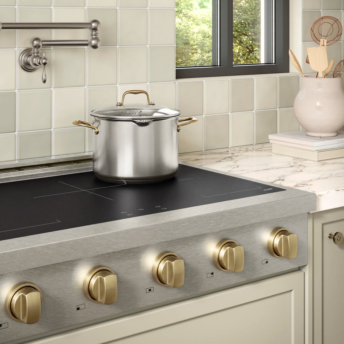 Induction rangetop with dark glass cooktop and gold-toned knob accents on satin stainless