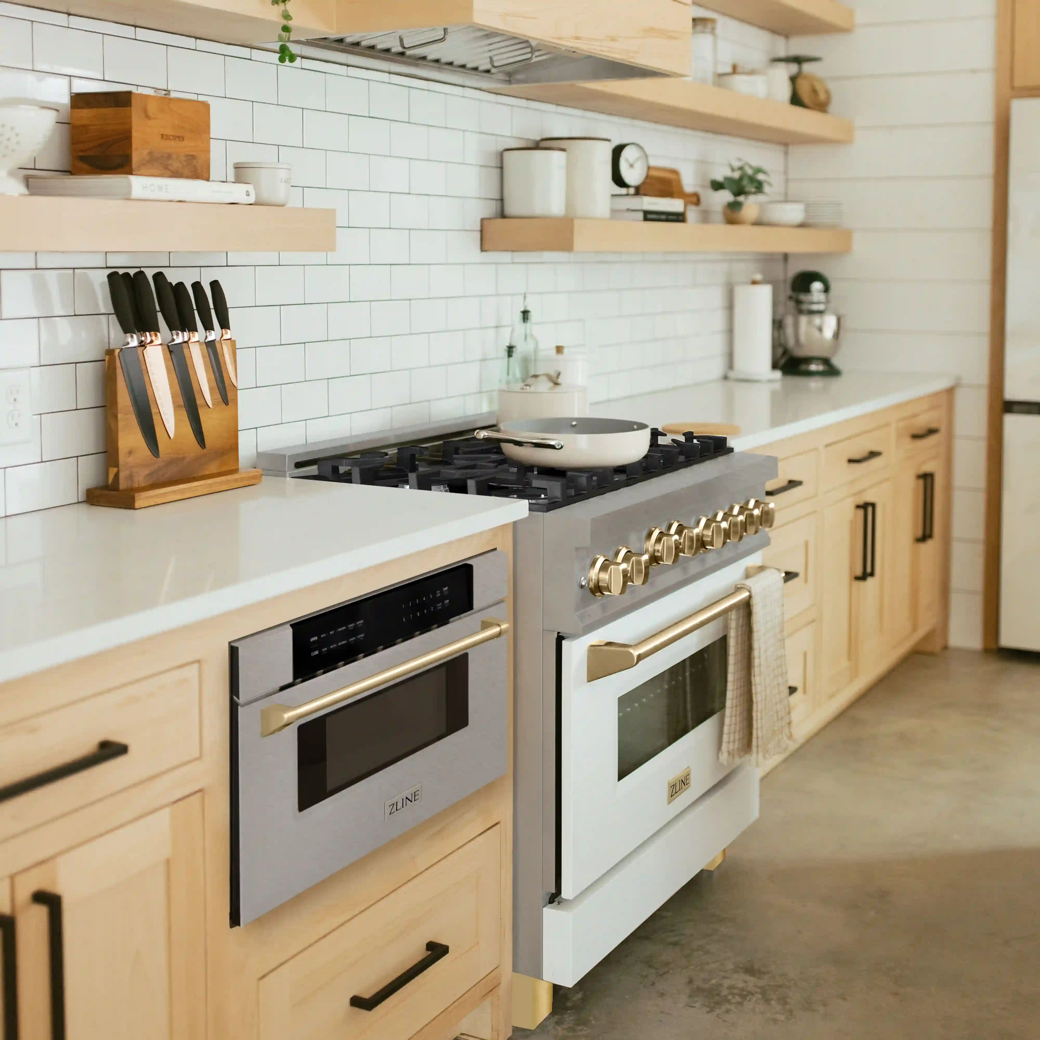 Stainless steel microwave drawer with gold handles installed in a modern kitchen