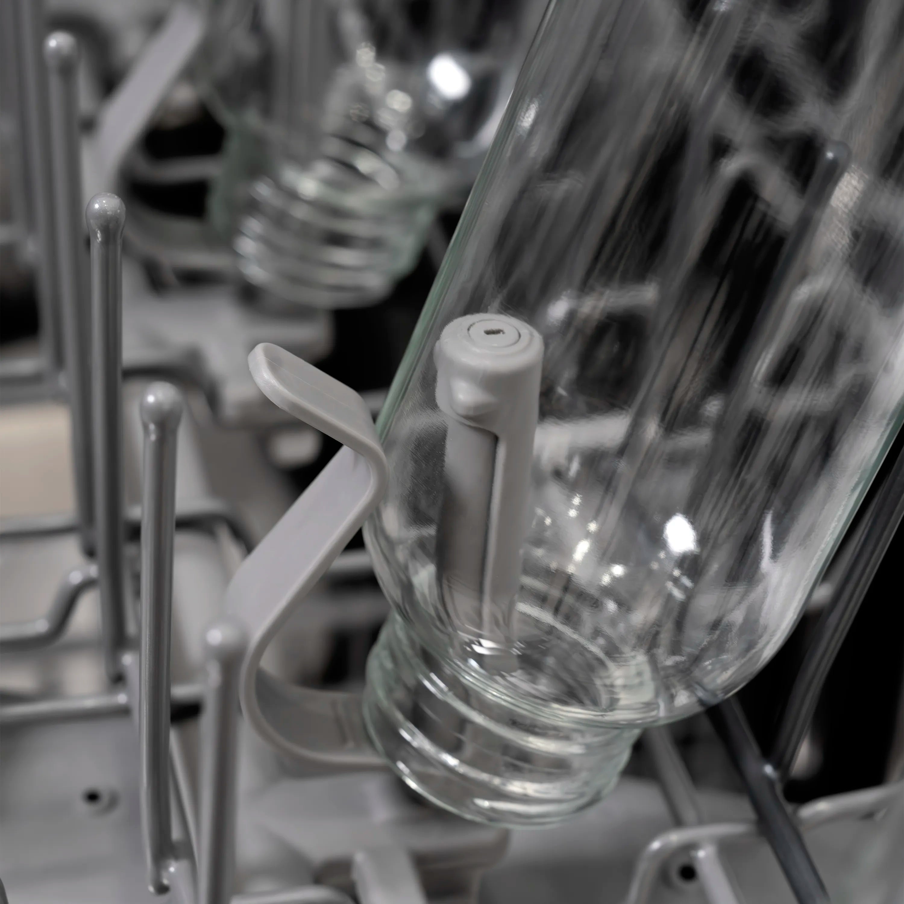 Dishwasher spray arm rinsing a glass cup inside the rack